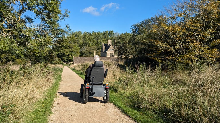 A visitor riding an off-road personal mobility scooter towards the manor at Lyveden.